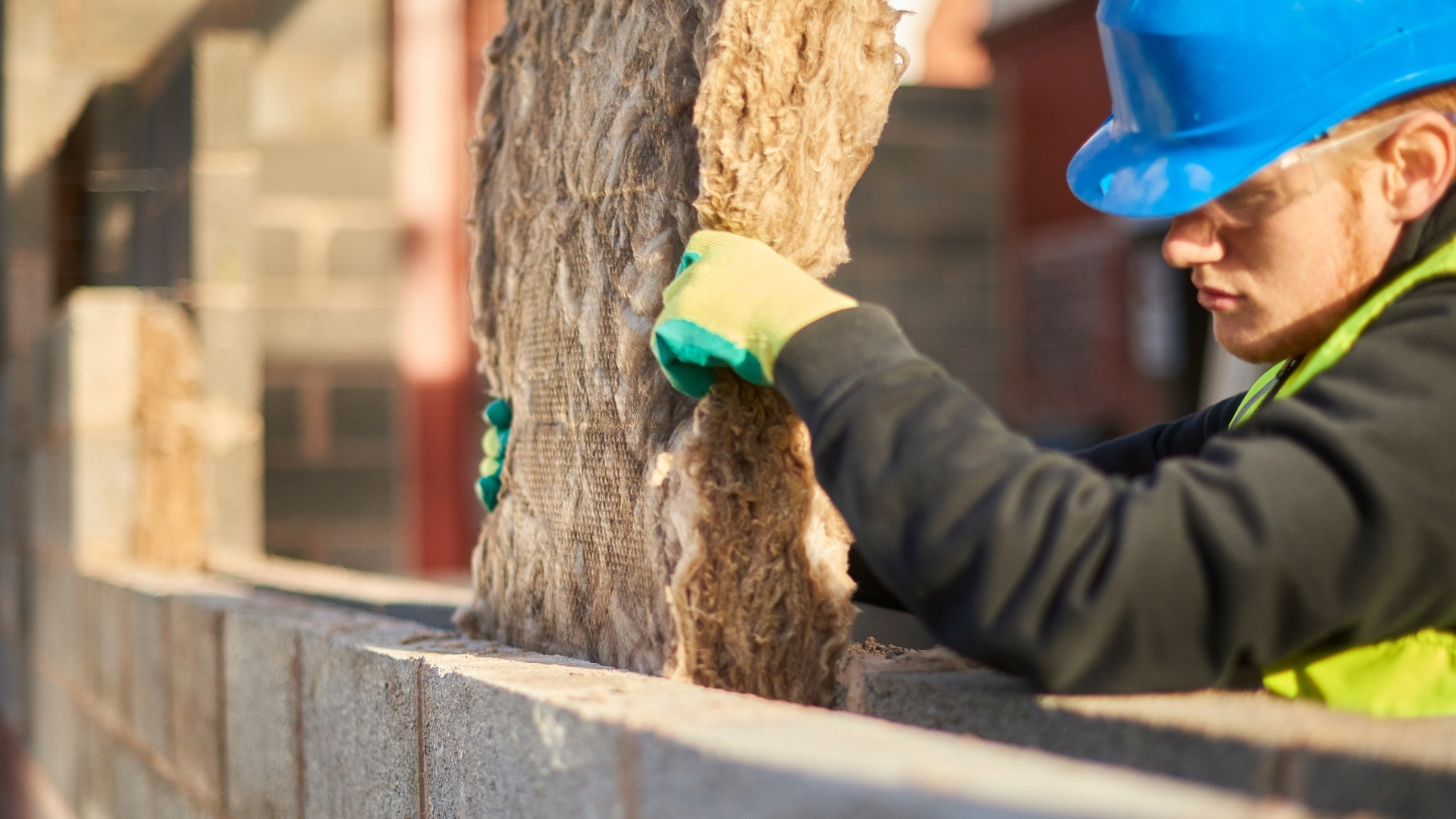 Engineer wearing a blue hard hat installing cavity wall insulation between two brick walls.